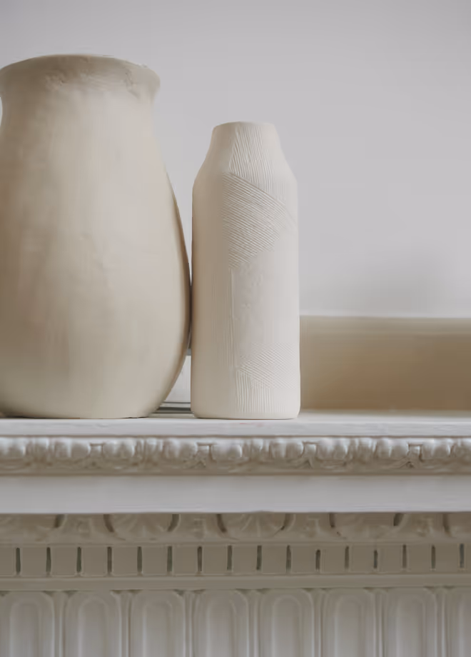 Two minimalist ceramic vases standing on a white decorative mantelpiece.
