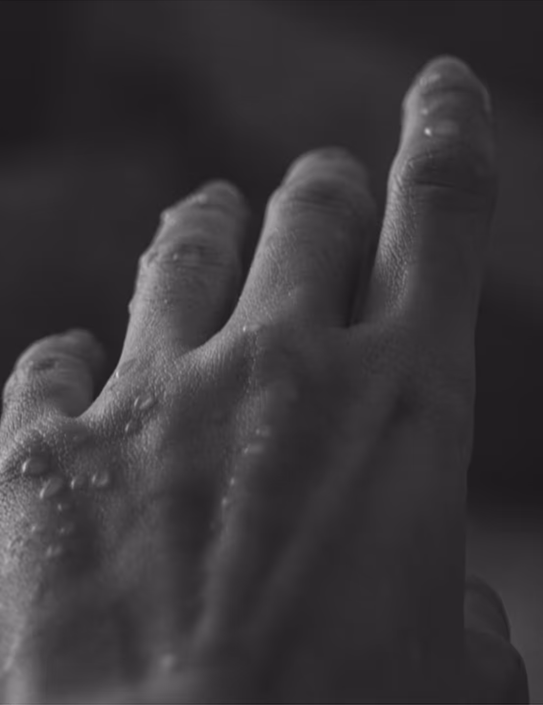 Black-and-white close-up of a hand with water droplets on the skin between the fingers.