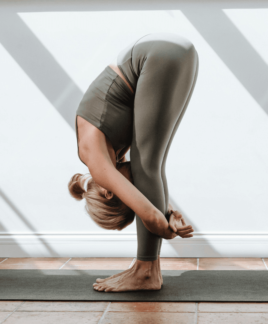 Woman performing a standing forward-fold yoga pose on a mat.