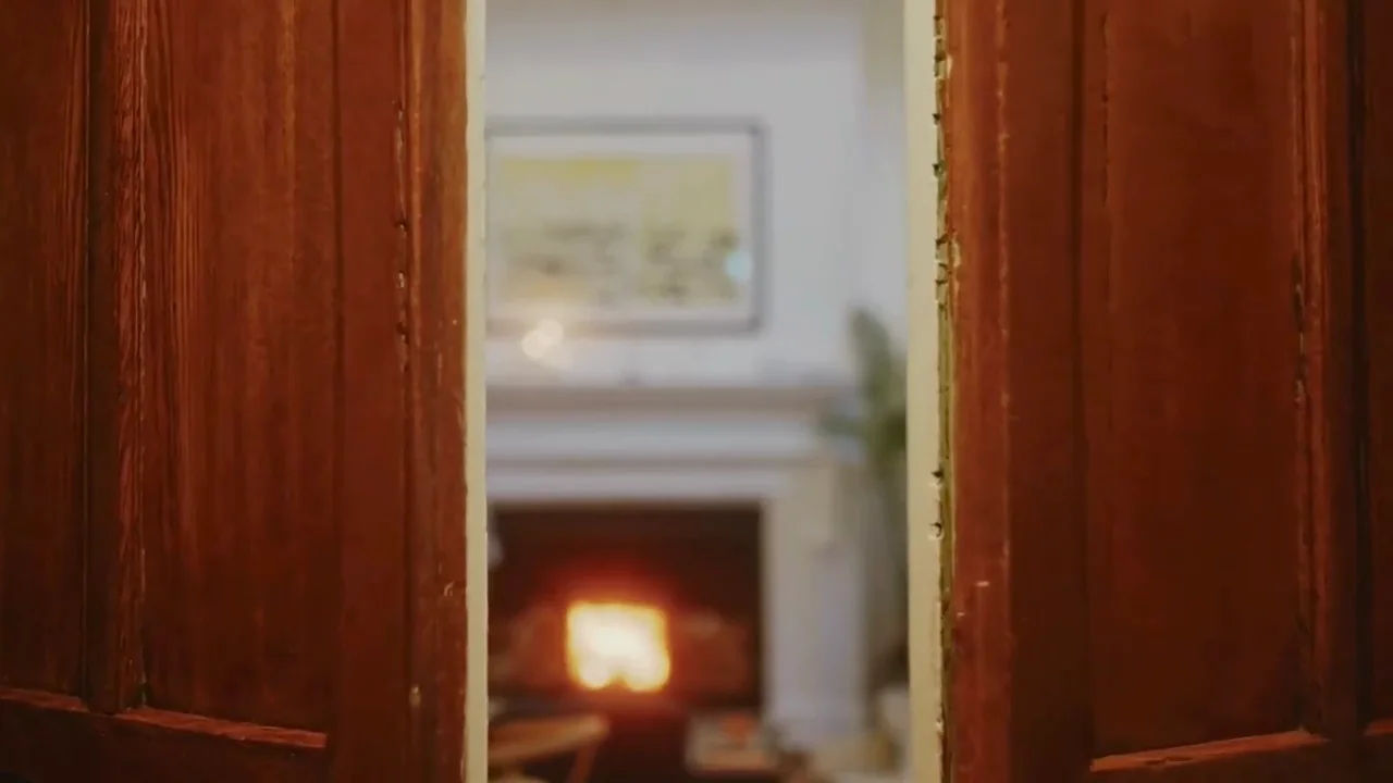 Panelled wooden doors opening onto a lamplit room with a fire
