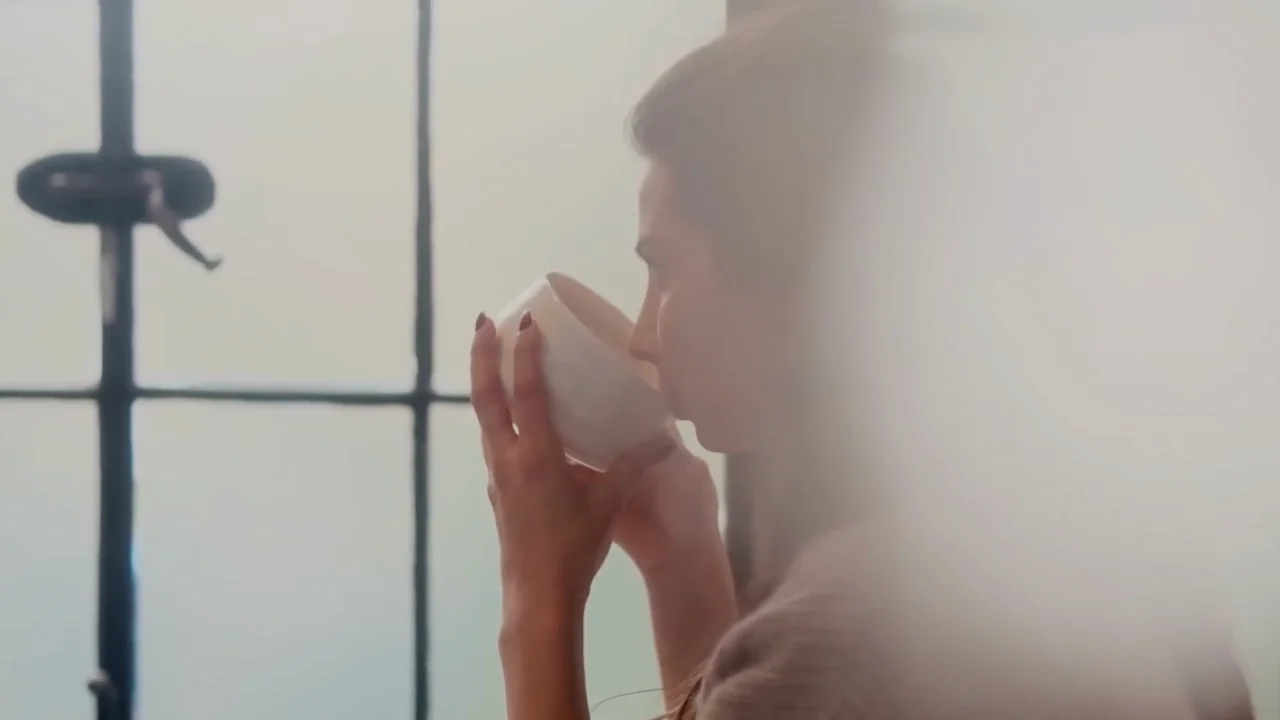 A woman drinking tea beside a misted window in soft morning light